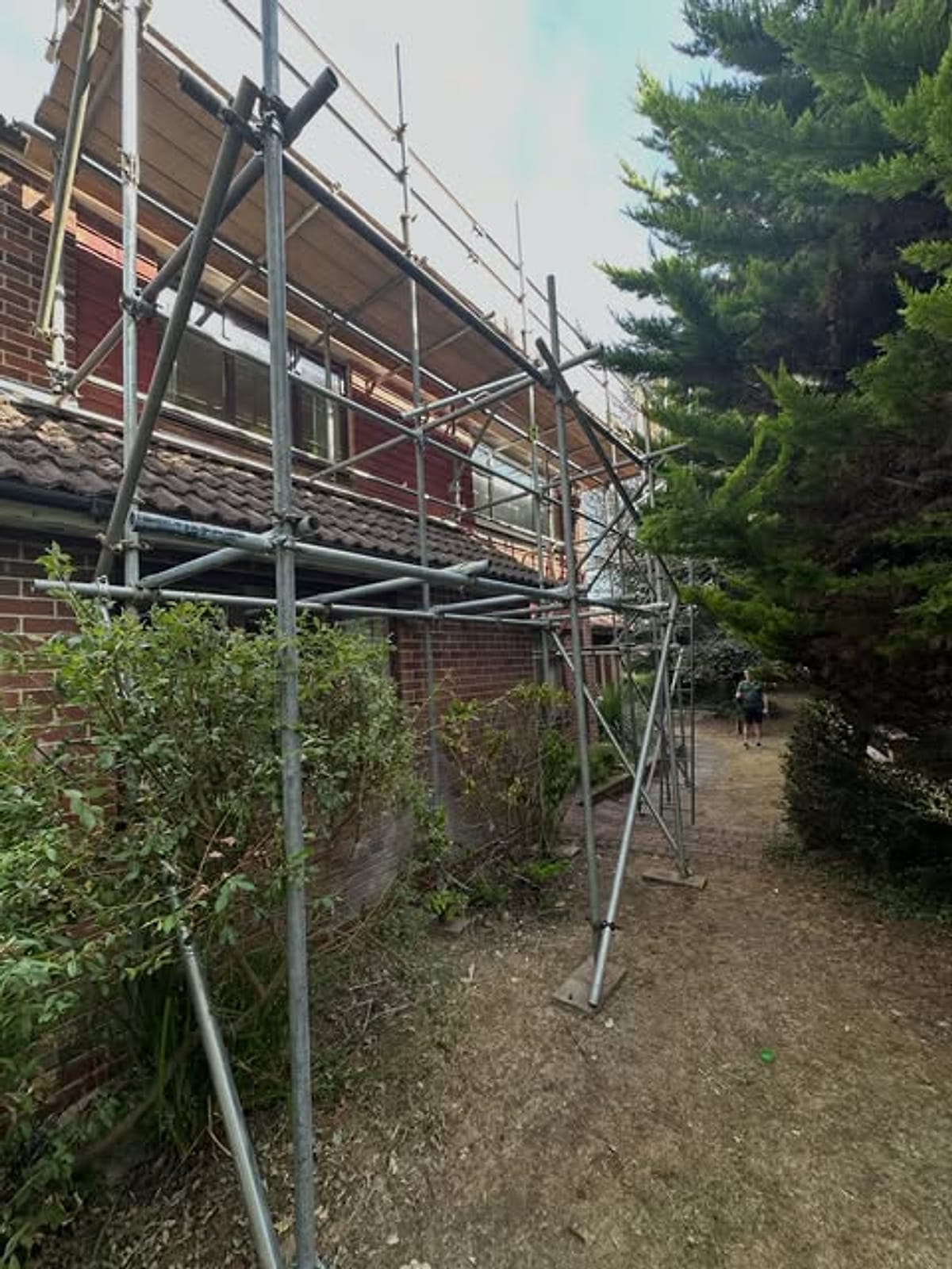 Scaffold bridged over a narrow side passage on adjustable base plates beside a house