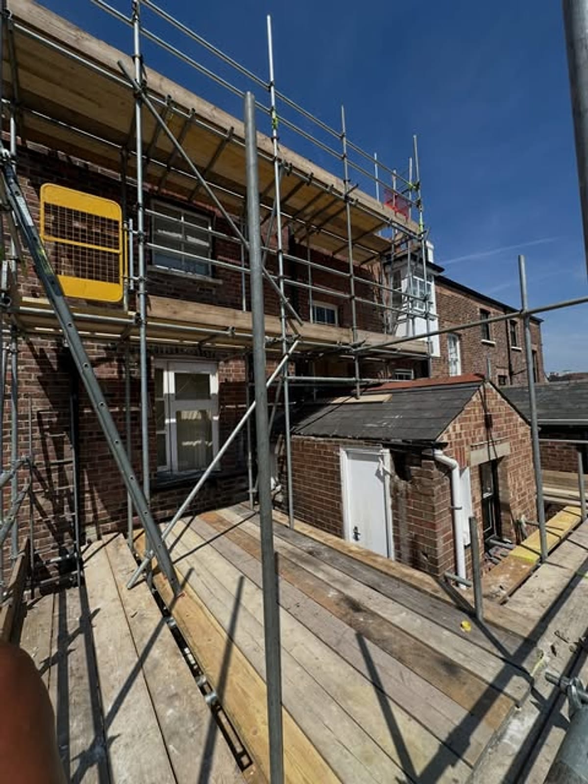 Fully boarded scaffold deck with guardrails and edge protection at first floor level