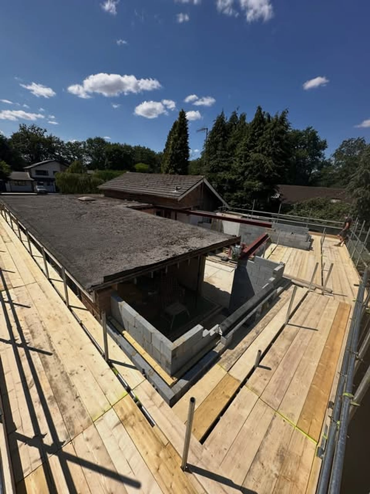Fully boarded scaffold deck laid out over a flat roof with a new opening formed below