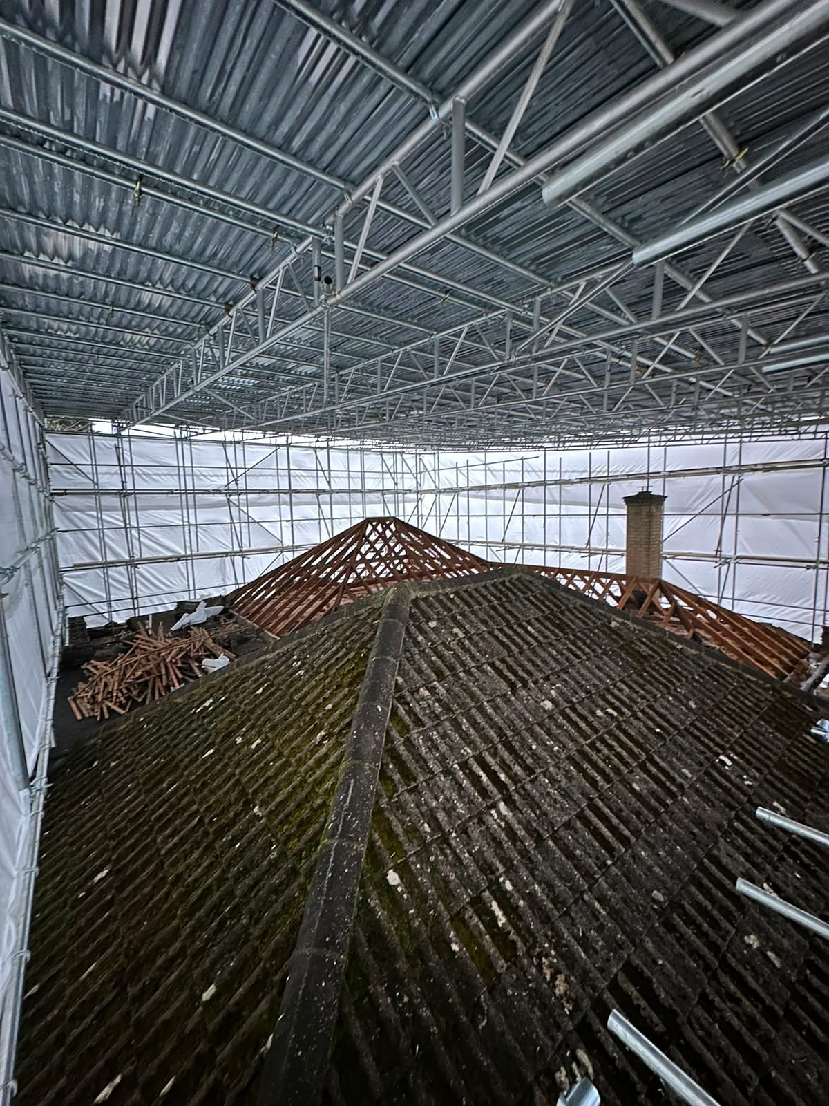 Underneath a temporary roof, aluminium beams and sheeting spanning over a stripped tiled roof